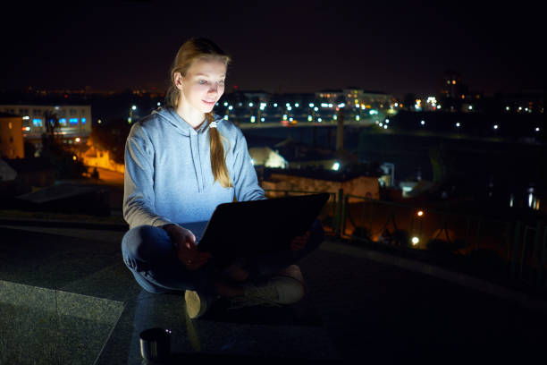 istock Young white man sitting outdoors and working with laptop in night, 1048375964