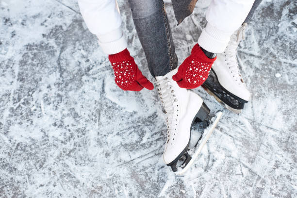 fille attacher lacets sur patins à glace avant de patiner sur la patinoire, les mains dans les gants de tricot rouges. - patinage sur glace photos et images de collection