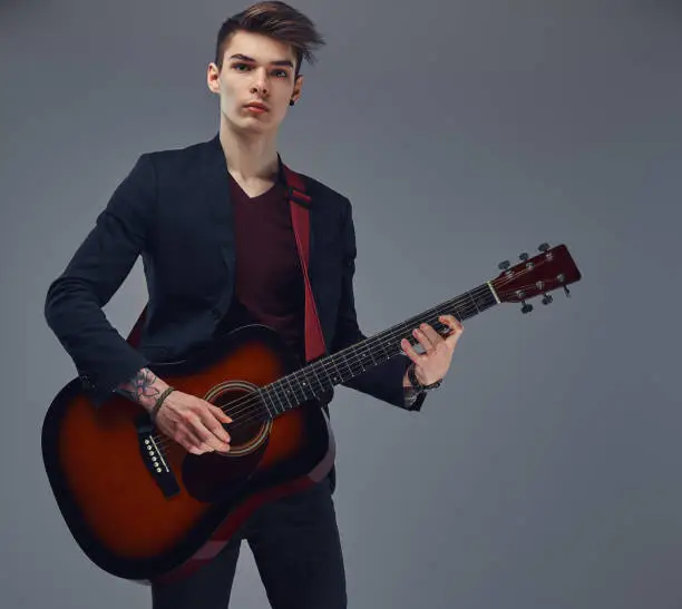 Photo of Handsome young musician with stylish hair in elegant clothes, playing on an acoustic guitar.