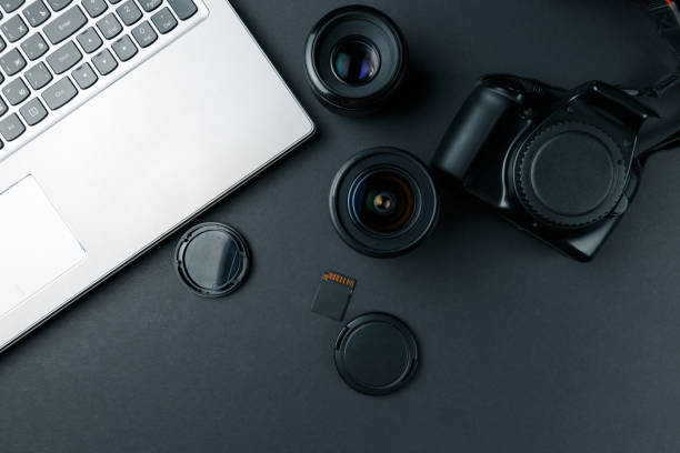 istock Work space on black table of photographer. Minimal workspace with Laptop, camera and lens copy space on dark background. Modern and elegant. Top view. Flat lay style. 1048390266