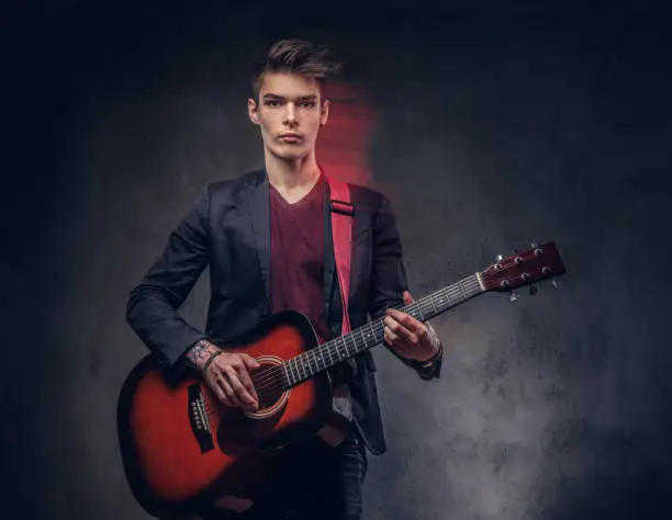 Photo of Stylish young musician with stylish hair in elegant clothes, playing on an acoustic guitar.