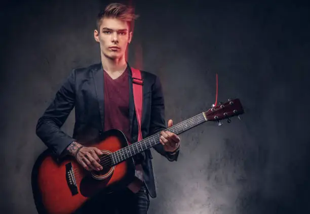 Photo of Stylish young musician with stylish hair in elegant clothes, playing on an acoustic guitar.