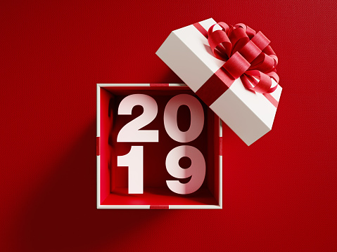 2019  is coming out of a white gift box tied with red ribbon on red background. Horizontal composition with copy space. Directly above. Great use for Christmas related gift concepts.
