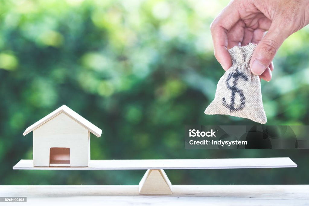 Balance home and money, home loan, reverse mortgage concept. Balance home and money, home loan, reverse mortgage concept : A man hand put us dollar money bag into scales on table with green nature as background. Savings, investment, loan for plan in the future. Domestic Life Stock Photo