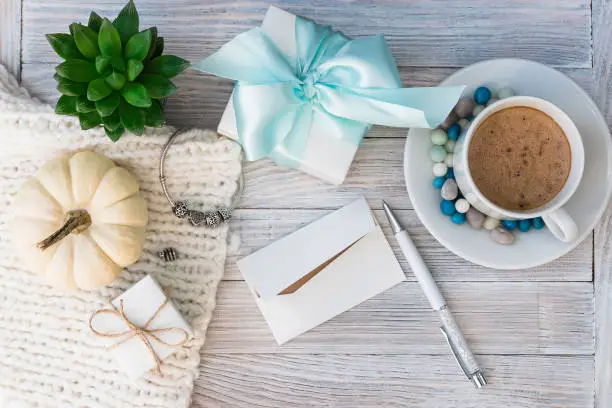 A cup of coffee and colored candies, jewelry boxes, a bracelet with silver charms, succulent and a white decorative pumpkin. Holiday gift with a note.