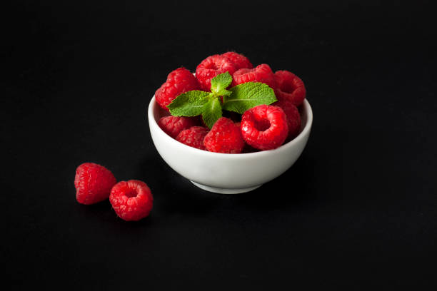 istock Fresh raspberries in a bowl with mint on black background 1048451626