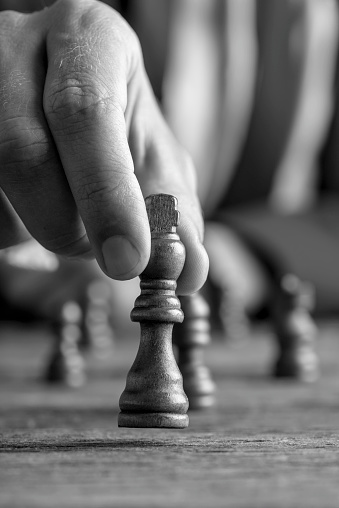 Greyscale image of a businessman playing chess moving black king piece lifting it up in his fingers in a close up view.