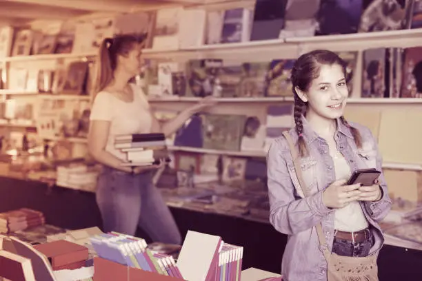 Female teenager is choosing book while chatting in bookstore.