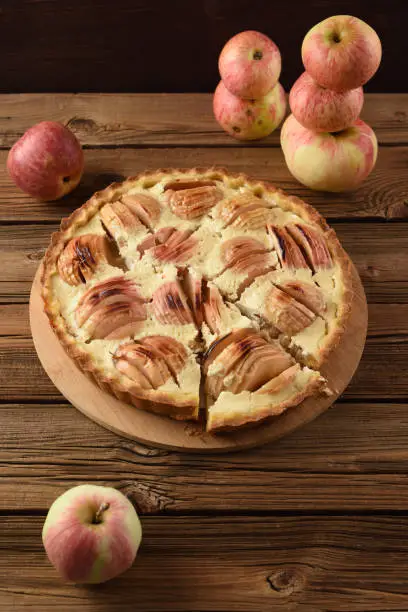 Homemade apple pie with cream filling served with organic apples on old wooden background copyspace