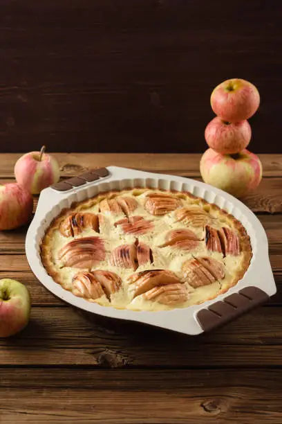 Homemade apple pie in baking dish served with raw organic apples on old wooden background copyspace