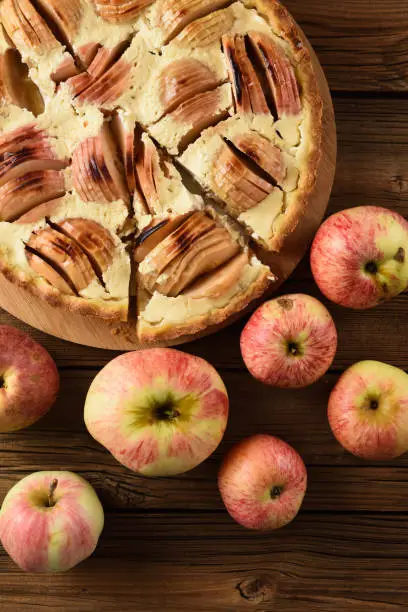 Tasty homemade apple tart with rich cream filling served with organic apples on old wooden background overhead view
