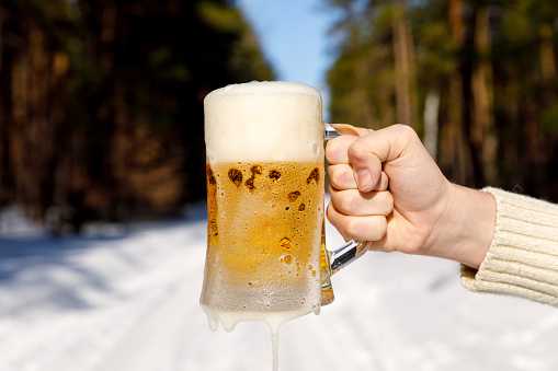 Glass of beer in hand on background of a winter forest.