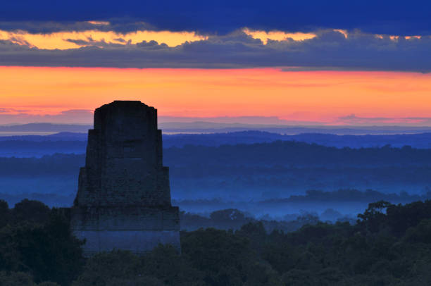 View of a sunrise above the Peten jungle with the pyramids of Tikal towering above the tree canopy in Guatemala. stock photo