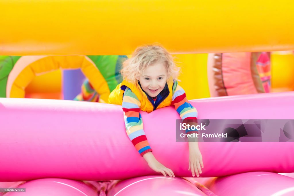 Child jumping on playground trampoline. Kids jump. Child jumping on colorful playground trampoline. Kids jump in inflatable bounce castle on kindergarten birthday party Activity and play center for young child. Little boy playing outdoors in summer. Amusement Park Stock Photo