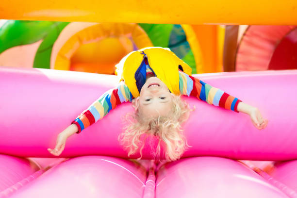 Child jumping on colorful playground trampoline. Kids jump in inflatable bounce castle on kindergarten birthday party Activity and play center for young child. Little boy playing outdoors in summer.