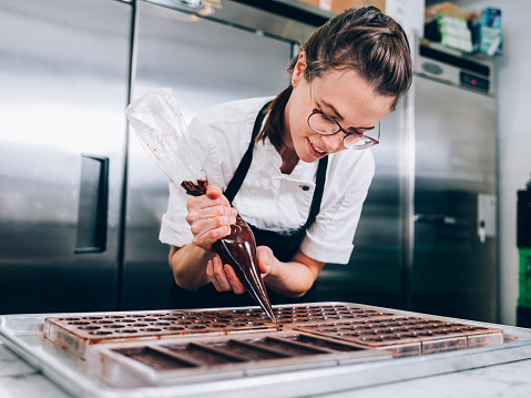 Location Portrait of female Chocolatier  prepping ingredients for chocolate making, in her commercial grade kitchen.