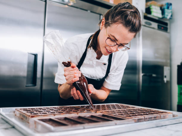 Young Master Chocolatier Location Portrait of female Chocolatier  prepping ingredients for chocolate making, in her commercial grade kitchen. baker occupation stock pictures, royalty-free photos & images