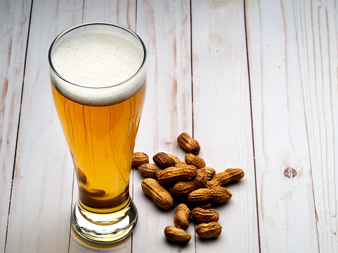 Pilsner of light beer with peanuts on light wooden table