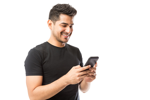 Handsome young man smiling and social networking on his smartphone over white background
