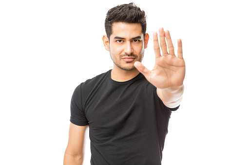 Portrait of serious young man making stop gesture against white background