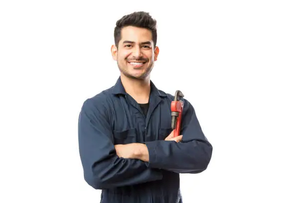 Portrait of smiling young male plumber with pipe wrench standing arms crossed on white background