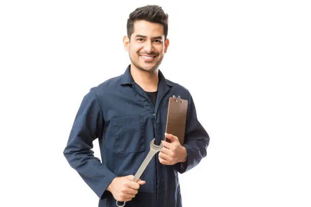 Portrait of smiling male repairman holding wrench and clipboard over white background