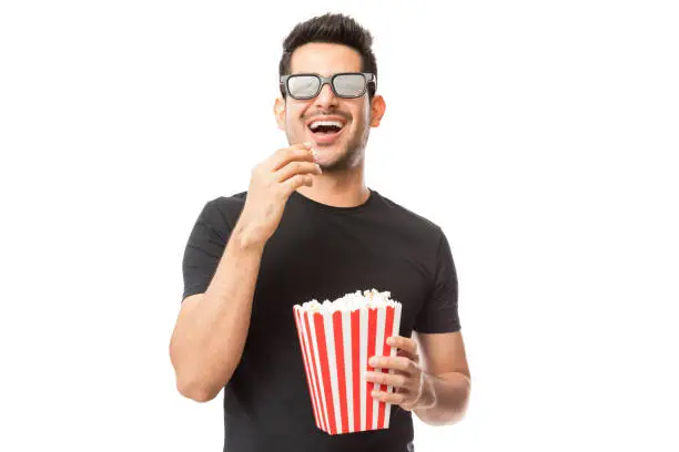 Photo of Smiling Young Man Watching 3D Movie While Eating Popcorn