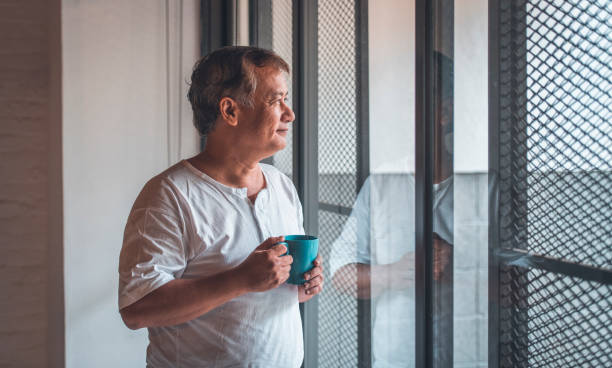 gentil homme senior avec une tasse de café par la fenêtre - homme mug regarder dehors photos et images de collection