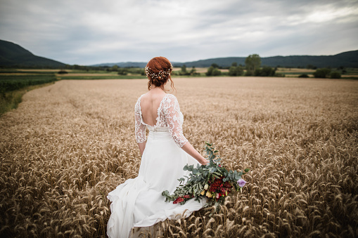 Stunning young bride with bouquet of wedding flowers standing in the wheat field