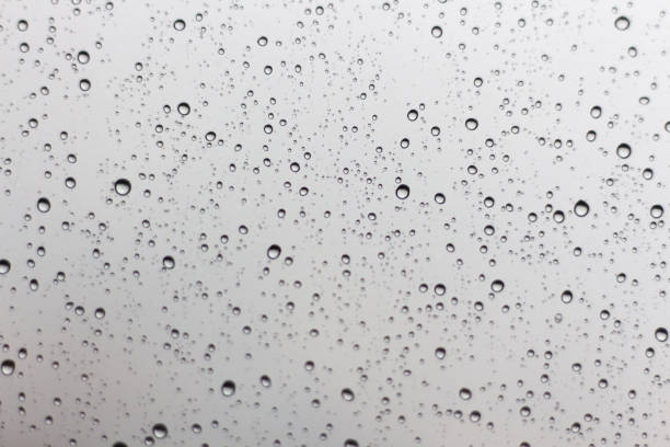 istock Rain drops on window glasses surface with cloudy background . Natural Pattern of raindrops isolated on cloudy background. 1048590156