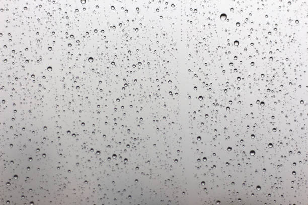istock Rain drops on window glasses surface with cloudy background . Natural Pattern of raindrops isolated on cloudy background. 1048590172