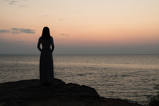 Silhouette of a girl on a sunset background (sunrise) on the sea, horizon line. Summer walk on the beach.