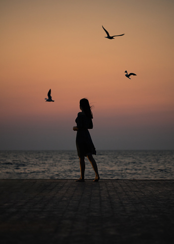 Silhouette of a girl on a sunset background (sunrise) on the sea, horizon line. Summer walk on the beach.