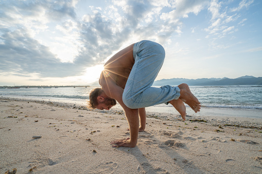 Healthy young man exercising yoga outdoors on the beach at sunrise in a tropical climate, Bali, Indonesia. People healthy balance concept