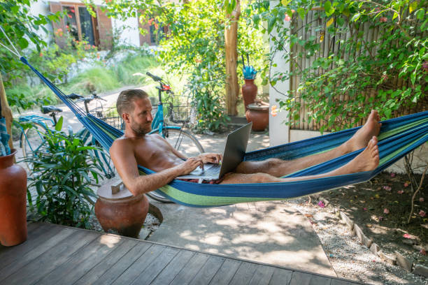 istock Young man on hammock relaxing on patio with a computer in a tropical place enjoying vacations and relaxation time 1048638610