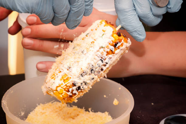 Chef sprinkles corn on top with cheese, cooked on a grill and bathed in sauce