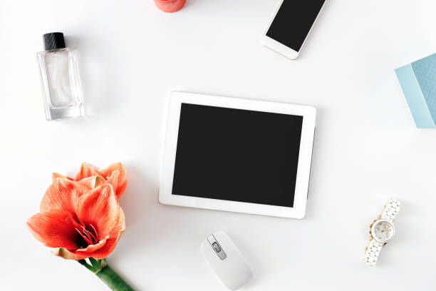 Flat lay, top view office table desk. Feminine desk workspace with flower amaryllis, tablet with blank screen, smartphone, womens wristwatch and female perfume