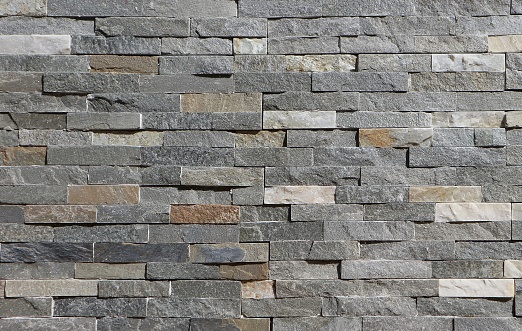 Stone wall cladding made of horizontal gray, brown and white strips of rock stacked . Background and texture
