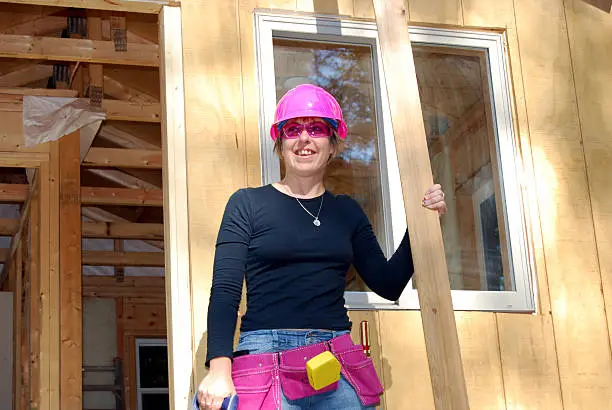 female carpenter/construction worker with pink hard hat, glasses and toolbelt