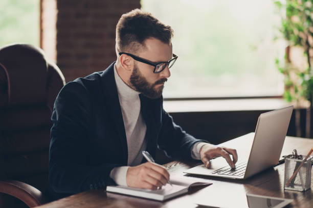 istock Elegant classic smart clever intelligent handsome attractive confident bearded ceo in black jacket and glasses, typing in laptop, writing start-up project strategy at modern work place, station 1048677712
