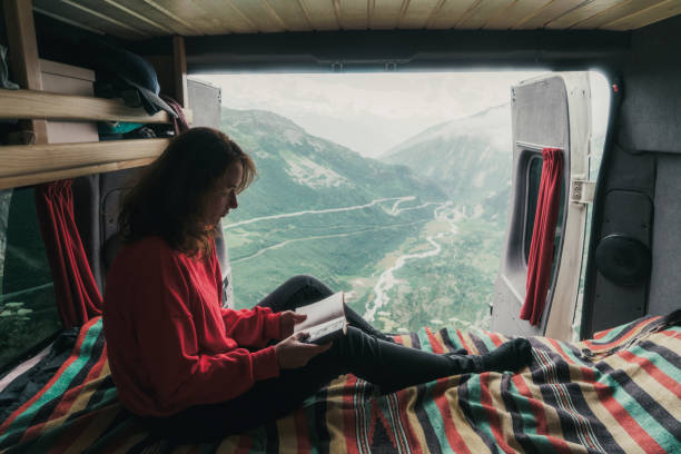 Woman reading book in camper van with view on Furka Pass Young Caucasian woman reading book in camper van with view on Furka Pass furka pass photos stock pictures, royalty-free photos & images