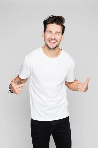 Portrait of cheerful young man pointing at himself on grey background