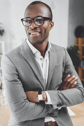 smiling african man with arms crossed looking away at office space