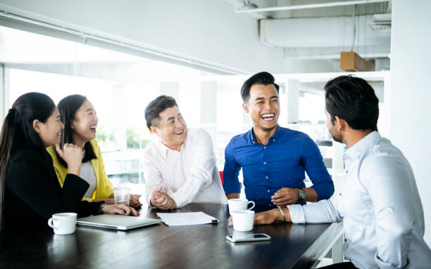 Business people laughing in meeting Multi racial business people with laptop on table, sitting together and smiling malaysia office workers stock pictures, royalty-free photos & images
