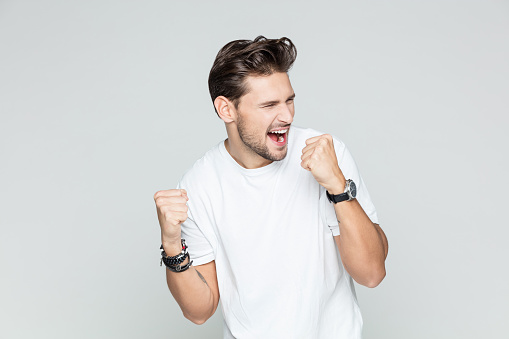 Portrait of young excited man celebrating success, looking away and cheering on grey background