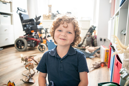 Cheerful boy with muscular dystrophy sitting on playroom floor, looking towards the camera, smiling