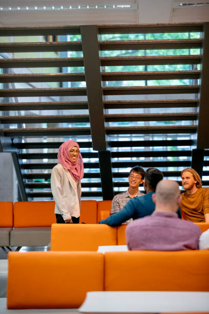 University Students Sharing Ideas A group of adult university students share ideas in the university lobby; they are all wearing casual clothing. common room stock pictures, royalty-free photos & images