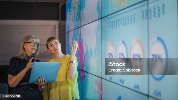 Businesswomen Discussing Ideas Against An Information Wall Stock Photo - Download Image Now