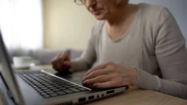 Old lady trying to type on laptop at home, computer courses, online training