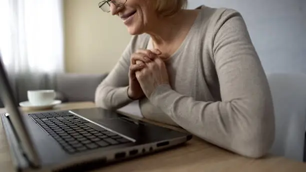 Elderly woman happy to see her children in internet, looking at laptop screen